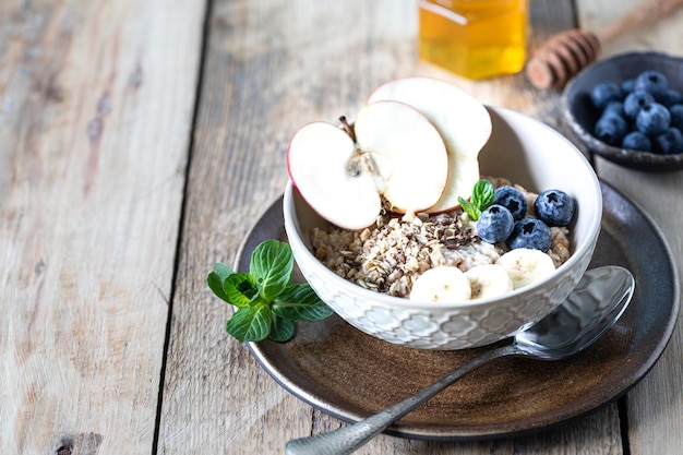 Desayuno saludable avena o granola con arándanos, manzana y miel sobre un fondo rústico de madera. Copiar espacio.