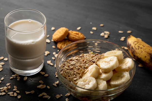 Desayuno saludable de avena con plátano, un vaso de leche y unas galletas en la mesa negra