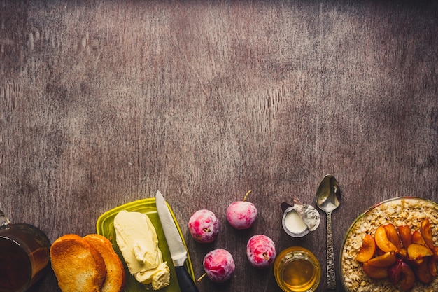 Desayuno saludable con avena en un recipiente de vidrio, ciruelas, miel, crema y una taza de té negro sobre fondo de madera oscura. Vista superior. Copie el espacio. Naturaleza muerta. Endecha plana. Entonado