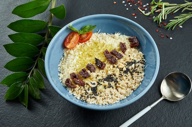 Desayuno saludable: avena con tomates secados al sol, parmesano y mantequilla en un recipiente azul sobre una superficie negra