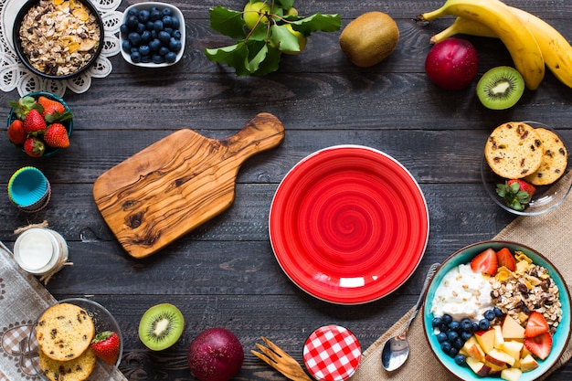 Desayuno saludable, cereal con yogurt, fresas, arándanos, manzana, plátano en madera