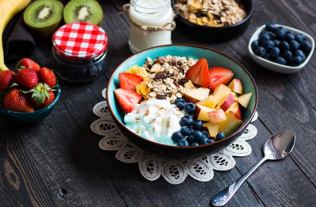 Desayuno saludable, cereales con yogur, fresas, arándanos, manzana, plátano, en madera rústica. Vista superior