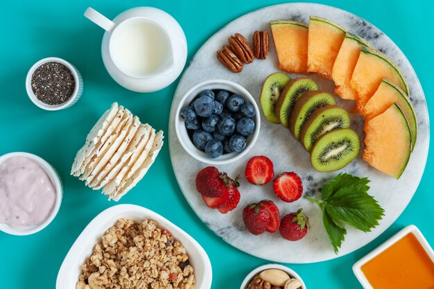 Desayuno saludable Charcuterie Boards - granola, yogur, variedad de frutas y bayas, nueces y hojuelas en el brillante fondo de verano