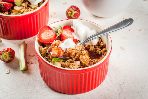 Desayuno saludable. Crumble de avena y granola con ruibarbo, fresas y moras frescas, semillas y helado en tazones horneados, decorados con menta, sobre mesa de piedra blanca de hormigón, copyspace