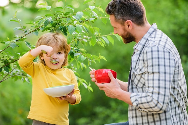 Desayuno saludable fin de semana desayuno por la mañana feliz día del padre Niño pequeño con papá come cereal Familia feliz juntos hijo y padre comiendo alimentos saludables al aire libre y haciendo dieta Productos lácteos