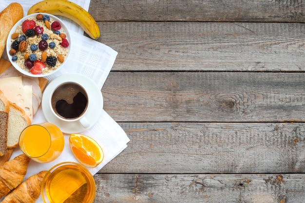 Desayuno saludable con frutas, bayas, nueces, café, huevos, miel sobre fondo de madera