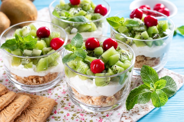 Desayuno saludable con frutas exóticas, yogur y galletas en un frasco de vidrio sobre un fondo de madera azul