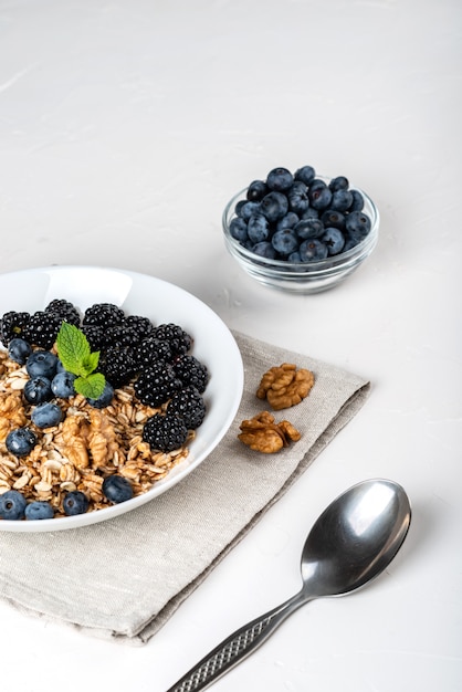 Desayuno saludable. Granola casera, muesli, cereales con moras, arándanos, nueces, miel y menta en un tazón blanco