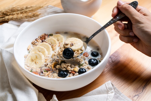 Desayuno saludable. Granola fresca, muesli con leche, bluberries y plátano en mesa de madera.