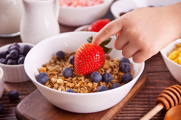 Desayuno saludable. Granola, muesli con frutos rojos frescos. La mano del niño toca una fresa.