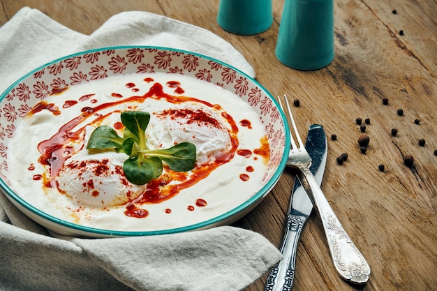 Desayuno saludable - huevo escalfado con salsa de yogur en un recipiente azul sobre una superficie de madera. Cilbir