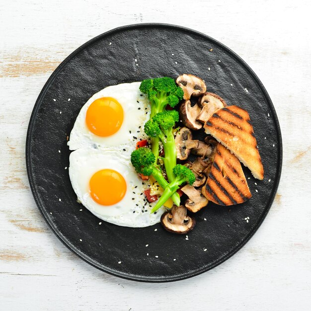 Desayuno saludable Huevo frito con brócoli, champiñones y pan En un plato de piedra negra Vista superior