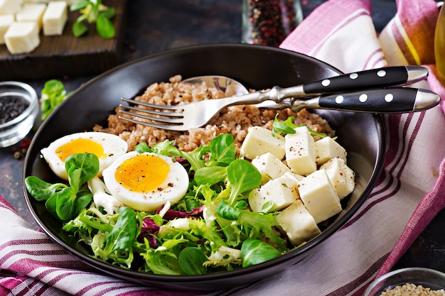 Desayuno saludable con huevo, queso, lechuga y gachas de trigo sarraceno en la oscuridad