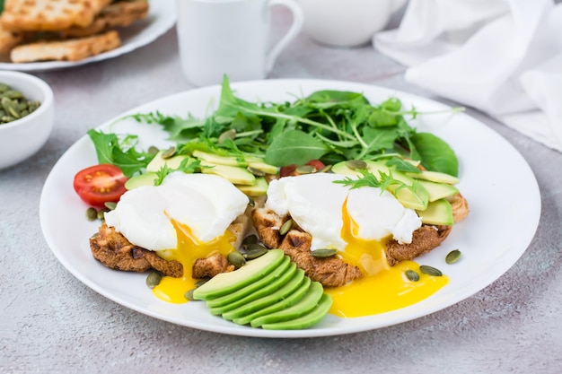 Desayuno saludable. Huevos escalfados sobre tostada con trozos de aguacate, rúcula, mizuna y hojas de acelga y tomates cherry en un plato sobre una mesa servida. Dieta flexetaria