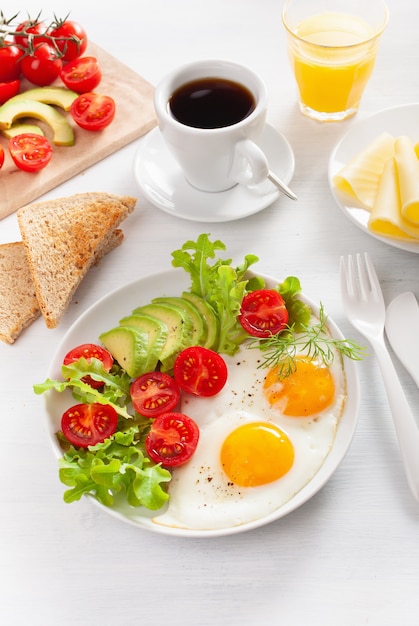 Desayuno saludable con huevos fritos, aguacate, tomate, tostadas y café.