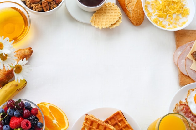 Desayuno saludable con muesli, frutas, bayas, nueces, café, huevos, miel sobre fondo blanco.