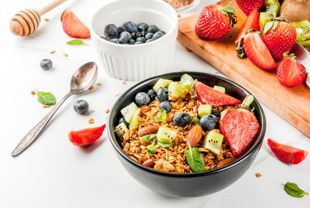 Desayuno saludable con muesli o granola con nueces y bayas y frutas frescas fresa, arándano, kiwi, en mesa blanca,