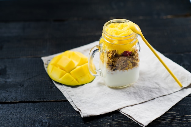 Desayuno saludable muesli y yogurt con batido de mango en frascos de vidrio.