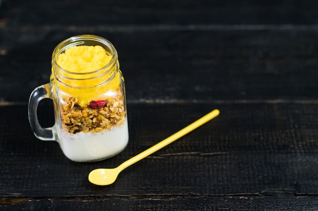 Desayuno saludable muesli y yogurt con batido de mango en frascos de vidrio.