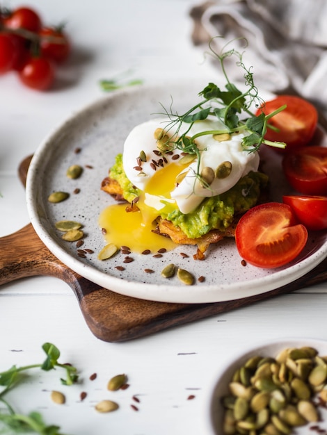 Desayuno saludable y nutritivo de panqueques de papa, puré de aguacate, huevo escalfado, brotes de guisantes y varias semillas en un plato de cerámica