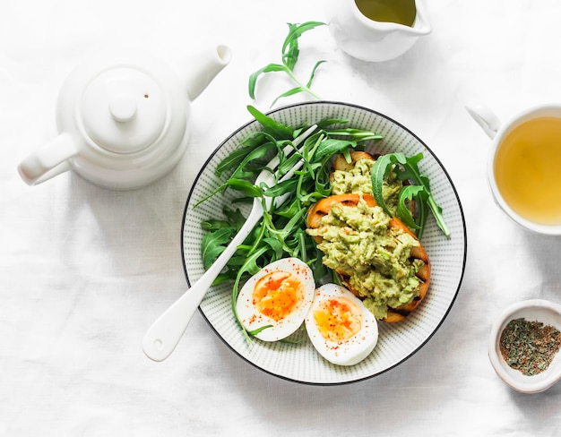 Desayuno saludable o merienda ensalada de rúcula de huevo cocido y tostadas de aguacate sobre un fondo claro