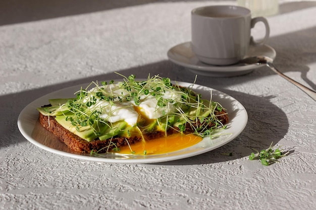 Desayuno saludable pan integral tostado con microgreens de huevo escalfado de aguacate y una taza de café