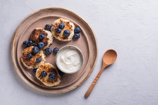 Desayuno saludable de panqueques de requesón, syrniki con arándanos y crema agria de cerca en un plato sobre la mesa