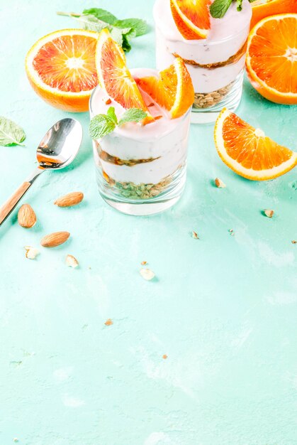 Desayuno saludable Parfait de naranja sanguina con yogurt de granola almendra y menta fondo azul claro