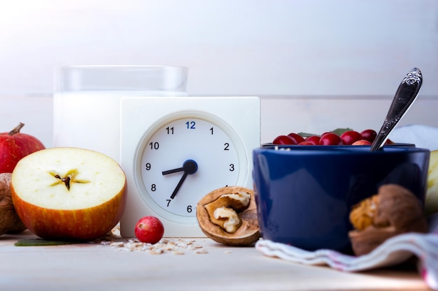 Desayuno saludable - reloj, leche, avena, arándanos, nueces, manzanas en una mesa de madera