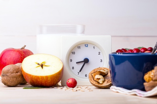 Desayuno saludable - reloj, leche, avena, arándanos, nueces, manzanas en una mesa de madera