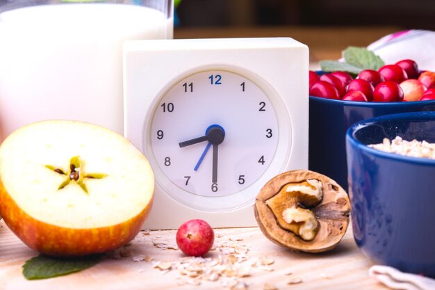 Desayuno saludable - reloj, leche, avena, arándanos, nueces, manzanas en una mesa de madera