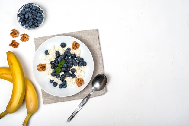 Desayuno saludable. Requesón con arándanos, nueces, miel y menta en un fondo de tazón blanco