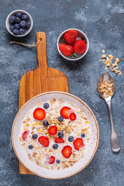 Desayuno saludable, tazón con granola de avena, leche y bayas, vista superior.