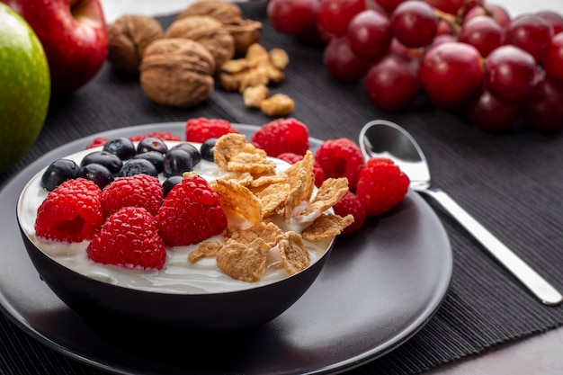 Desayuno saludable en un tazón con yogur y bayas y cereales rodeado de manzanas, nueces y uvas.