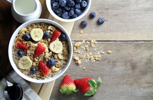 Desayuno saludable, tazón de yogurt con granola y fruta fresca en el fondo de madera