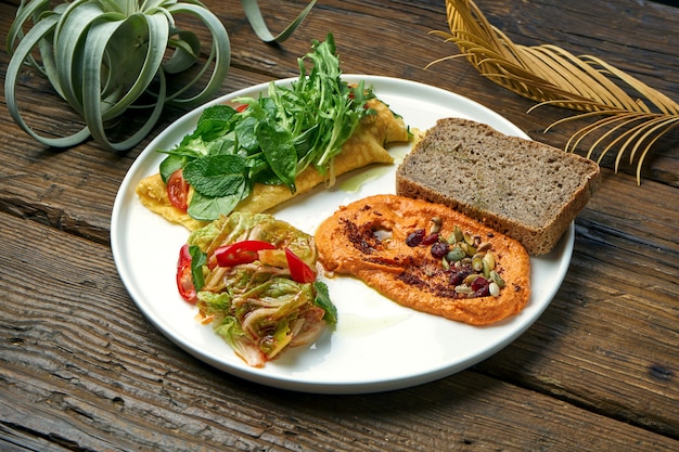 Desayuno saludable - tortilla con kimchi y hummus de pimientos al horno en un plato sobre una mesa de madera