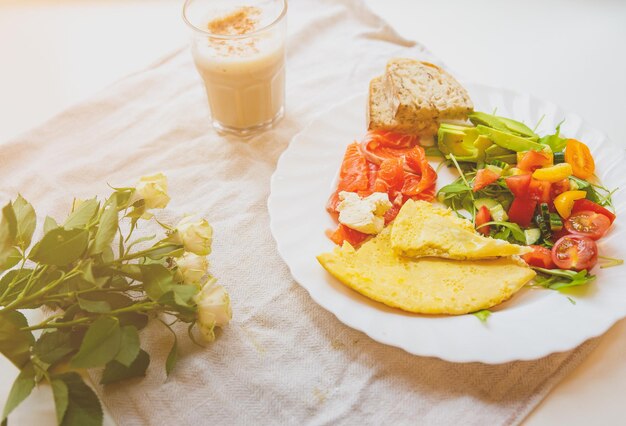 Desayuno saludable Tortilla con tomates y ensalada de rúcula Salmón con pan integral Capuchino y rosas sobre el fondo de lino rústico Ideal para la mañana