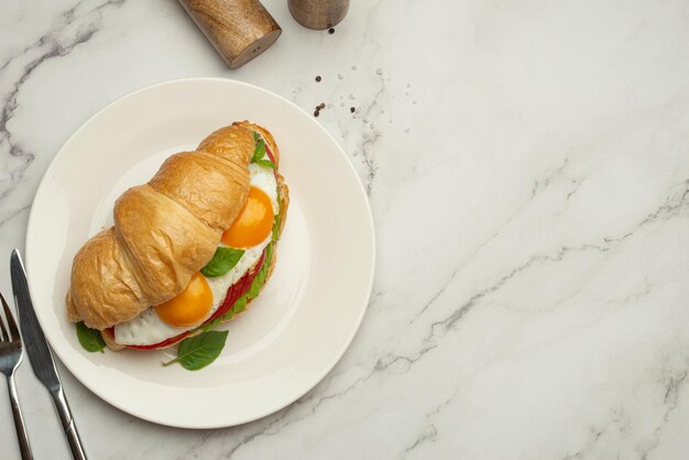 Desayuno saludable y útil Croissant con aguacate y huevos en una mesa gris