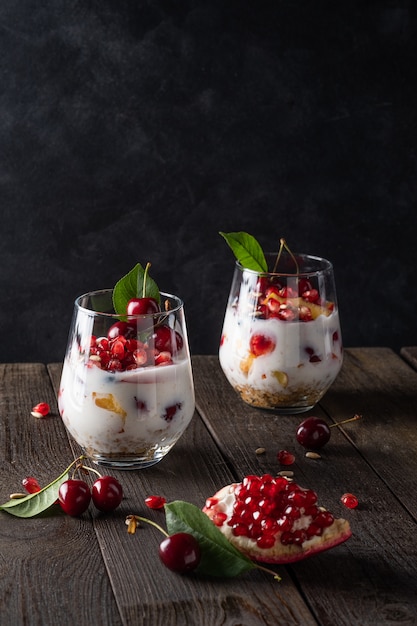 Desayuno saludable en un vaso con frutas frescas: granada, cereza, nectarinas, madreselva, yogur y granola sobre un fondo negro. Poca profundidad de campo con enfoque selectivo