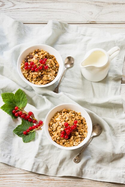 Desayuno saludable de verano para dos personas de granola, muesli sobre tabla de madera clara.