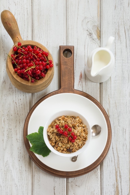 Desayuno saludable de verano de granola, muesli con jarra de leche con decoración de grosella roja en tablero ligero. Vista superior.