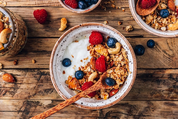 Desayuno saludable con yogur y granola horneada con bayas en dos tazones pequeños Granola horneada con nueces aceite de coco y miel