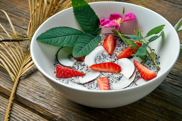 Desayuno saludable: yogurt con una mezcla de cereales, semillas de chia, fresas con leche de coco en un tazón sobre una madera