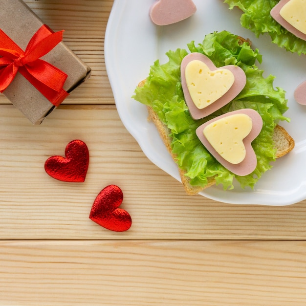 Desayuno para San Valentín. Sándwich de salchicha, queso y lechuga en la placa blanca.