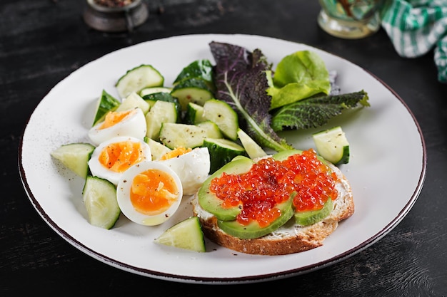 Desayuno Sándwich abierto saludable sobre tostadas con aguacate y caviar rojo huevos cocidos ensalada de pepino en plato blanco Alimentos proteicos saludables