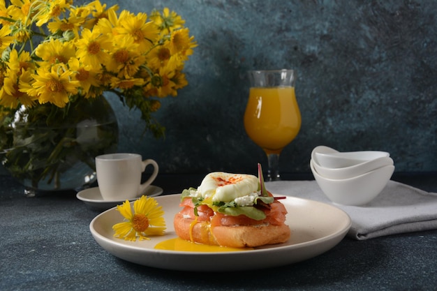 Desayuno con sándwich con pan de cereales y salmón, queso tierno y huevos escalfados y un vaso de jugo de naranja