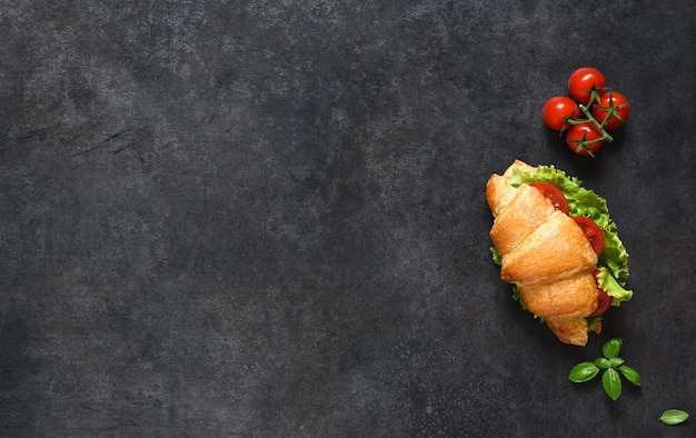 Desayuno con sándwiches de Croissant con Ensalada de Hojas, Jamón y Tomates Cherry, con salsa sobre fondo negro. Vista desde arriba.