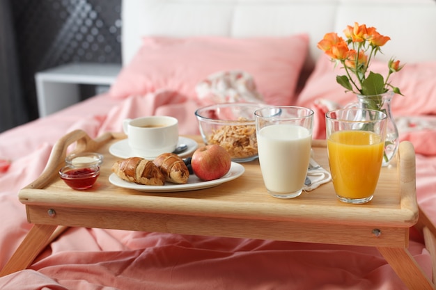 Desayuno servido en la cama en bandeja de madera con café y cruasanes.