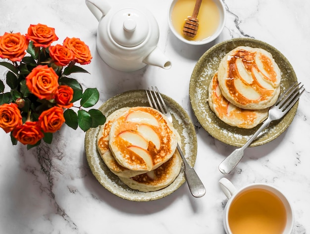 Desayuno servido tortitas con manzanas té verde un ramo de rosas sobre un fondo de mármol claro vista superior