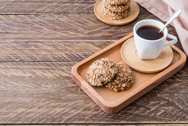 En el desayuno se sirven galletas dietéticas de avena con sésamo y semillas de lino en una bandeja de madera con café recién molido.